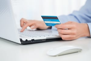 a close up shot of a person sitting at a laptop with a credit card in hand, entering details into the laptop